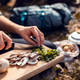 hands chopping mushrooms outdoors on a plank